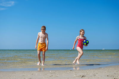 Full length of shirtless man on beach against clear sky