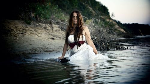 Portrait of young woman wearing white dress while standing in lake