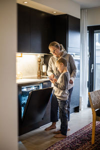 Mother teaching son to use mobile app while operating dishwasher in kitchen at home