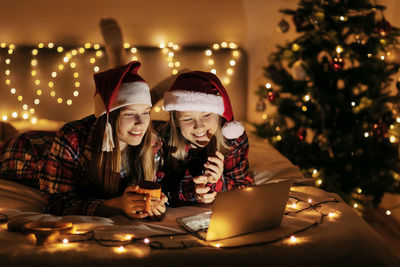 Two charming sisters lie on the bed with a laptop on christmas or new year's 