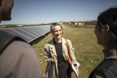 Smiling senior female entrepreneur talking with engineers while standing at power station