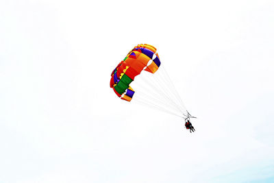 Low angle view of people parasailing against sky