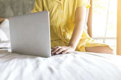 Midsection of woman using mobile phone on bed