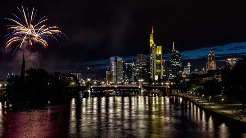 Firework display over river and illuminated buildings in city at night