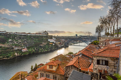 High angle view of buildings by river against cloudy sky
