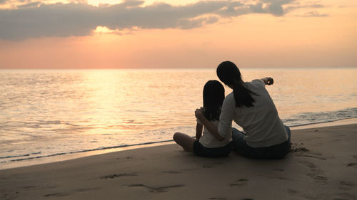 Men sitting on beach during sunset