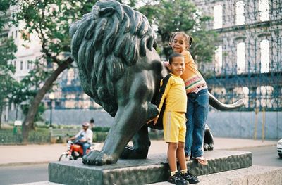 Full length of friends standing on sculpture in city