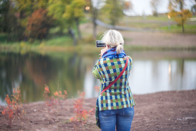 Rear view of woman photographing lake in mobile phone