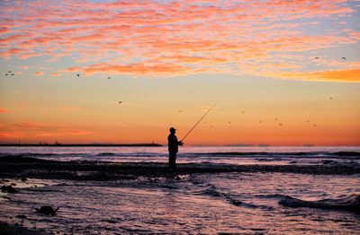 Silhouette man fishing in sea against sky during sunset