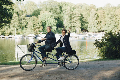 Senior couple enjoying tandem bike ride by pond in park