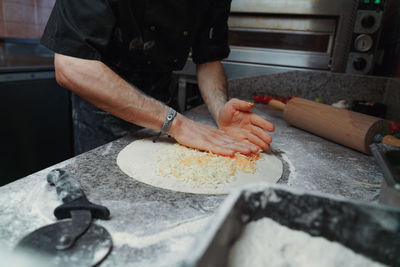 Midsection of man preparing pizza on table