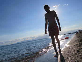 Full length of shirtless man walking on shore at beach against sky