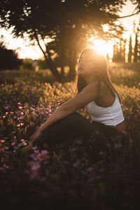 Young female sitting in the field among flowers at sunset