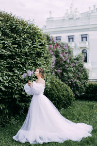 Beautiful bride in a wedding dress walks in a blooming apple-tree park in spring