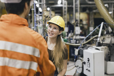 Smiling female manager wearing hardhat talking with male worker in factory