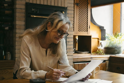 Woman calculating budget while standing in kitchen at home