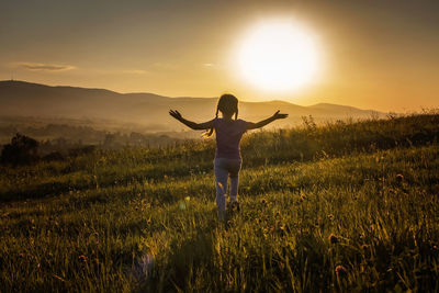 Rear view of woman standing on field against sky during sunset