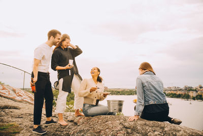 Rear view of friends sitting on rock against sky