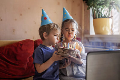 Cheerful kids blowing candles on cake indoors