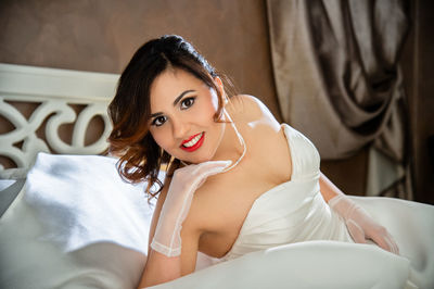 Portrait of smiling bride in dress sitting on bed at home