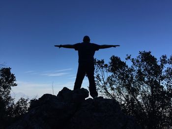 Silhouette of man with arms outstretched against clear blue sky