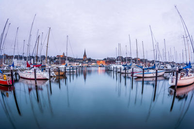 Sailboats moored at harbor against sky