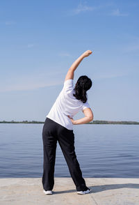 Rear view of woman standing by lake against sky