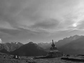 Stupa on mountain against cloudy sky during sunny day