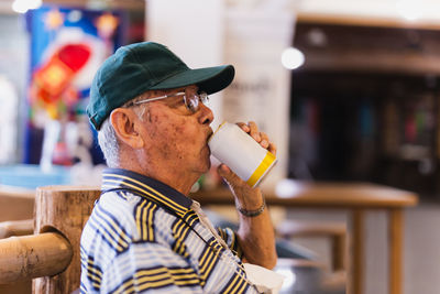 Side view ofsenior man drinking beer while sitting in a chair outdoor.