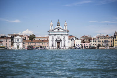 View of buildings by sea against sky in city