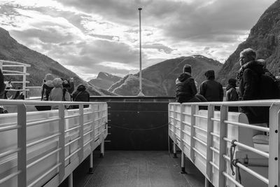 People sailing in passenger craft by mountains against sky