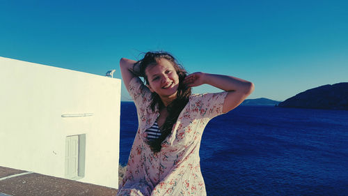 Portrait of smiling young woman standing against blue sky