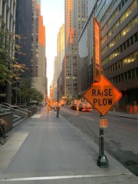 Road sign on street by buildings against sky during sunset