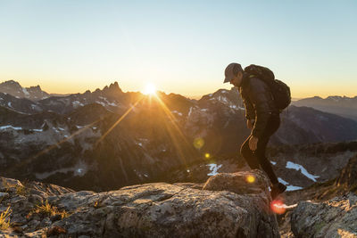 Backpacker scrambling over rocky terrain to reach mountain summit.