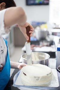 Cropped image of woman spreading cream on sponge cake at kitchen