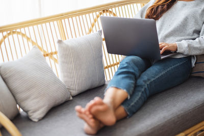 Midsection of woman using laptop while sitting on sofa at home