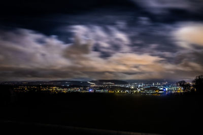 Illuminated cityscape by sea against sky at night