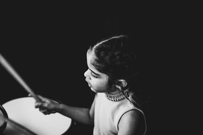 Girl playing musical instrument against black background