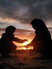 Silhouette people on shore against sky during sunset