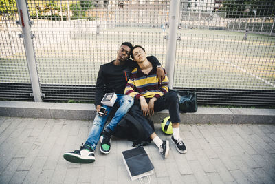 Full length portrait of young man with friend sitting against net