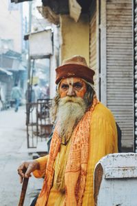 Close-up portrait of sadhu sitting against built structure in city