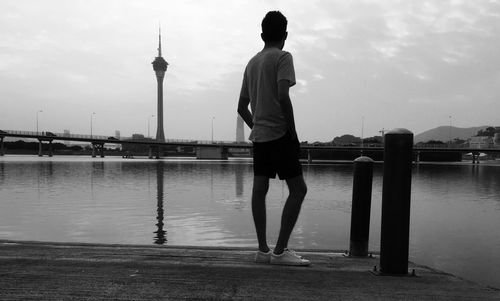 Rear view of man standing at pier over river against macao tower in city