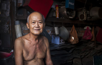 Portrait of smiling shirtless mature man sitting in warehouse