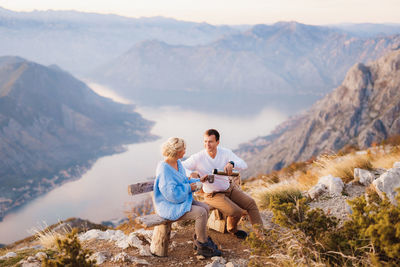 Friends sitting on rock against mountains