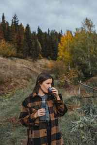 Young woman holding camera while standing by tree in forest