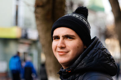 Close-up portrait of young man in warm hat outside on city urban background. happy millennial 