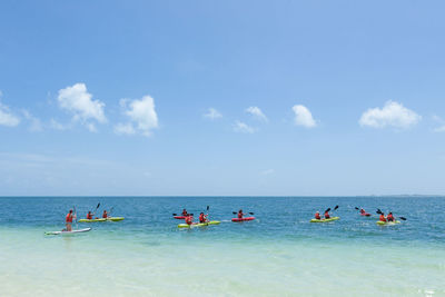 People kayaking in sea against cloudy sky