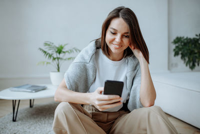 Young woman using mobile phone while sitting on sofa at home