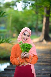 Portrait of a smiling young woman standing against plants