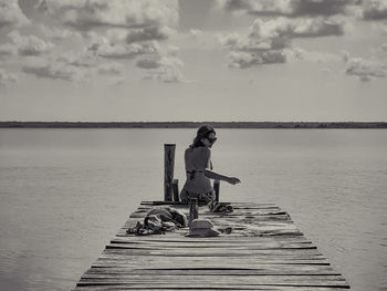 Rear view of woman wearing bikini sitting on pier over lake